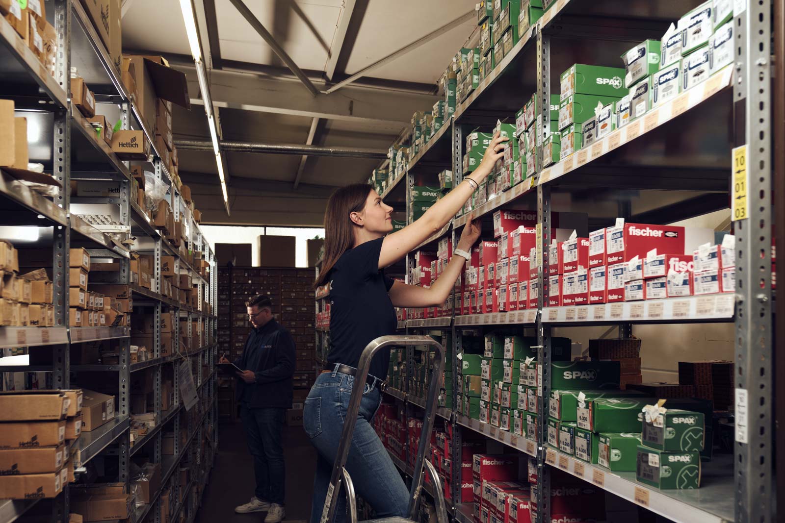 Mitarbeiterin holt Schrauben aus einem Regal